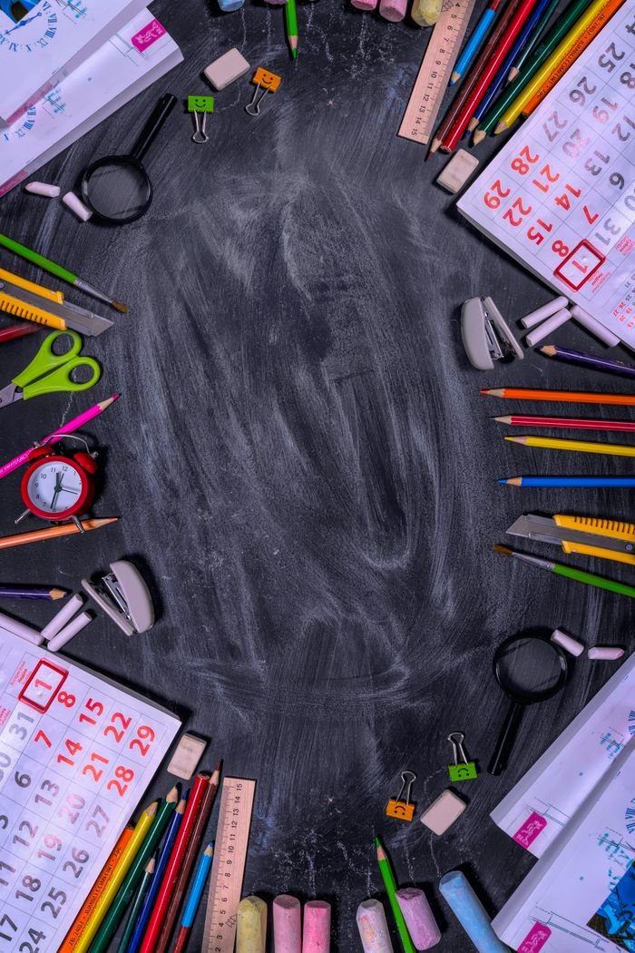 Flat lay of school stationery forming a frame on a blackboard surface.